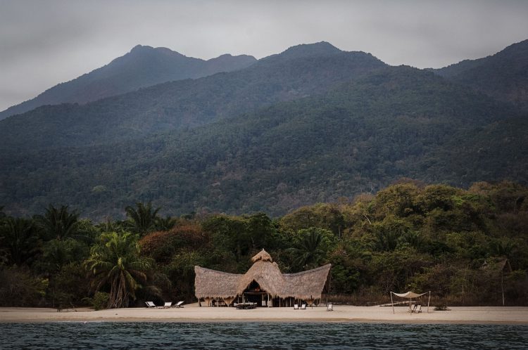 Das Meer, dahinter Strand mti einem Haus, dahinter grüne Berge