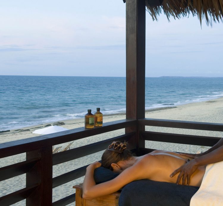 Eine Frau bekommt eine Massage auf einer Terrasse, daneben das Meer und Strand