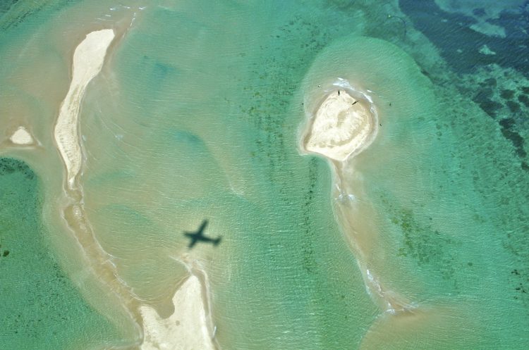 eine Aufnahme von oben: im Meer ein Schatten eines Flugzeuges