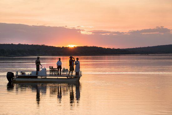 Personen unternehmen eine Bootstour auf dem Sambesi bei Sonnenuntergang