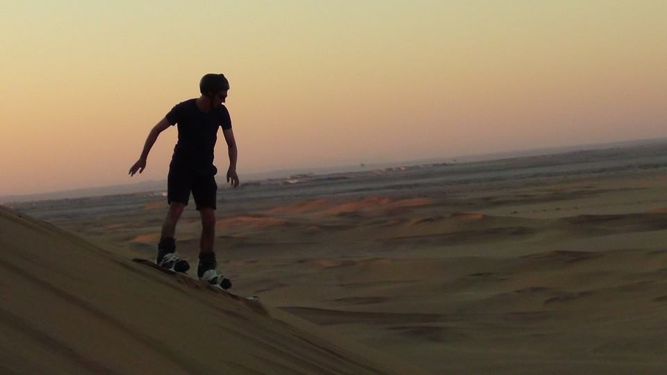 Person sandboarding in Namibia with a setting sun