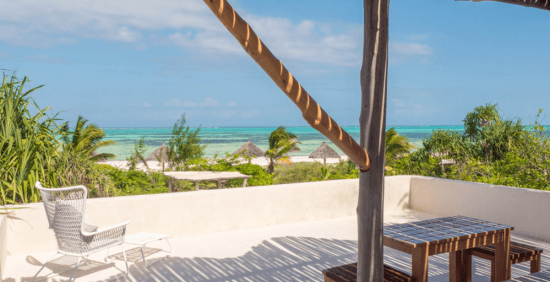 Eine Terrasse mit einem Tisch und einem weißen Sessel, dahinter der Strand