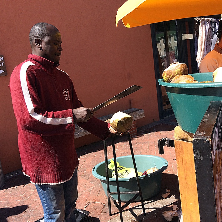 Homem corta coco em barraca no Old Biscuit Mill, Cape Town