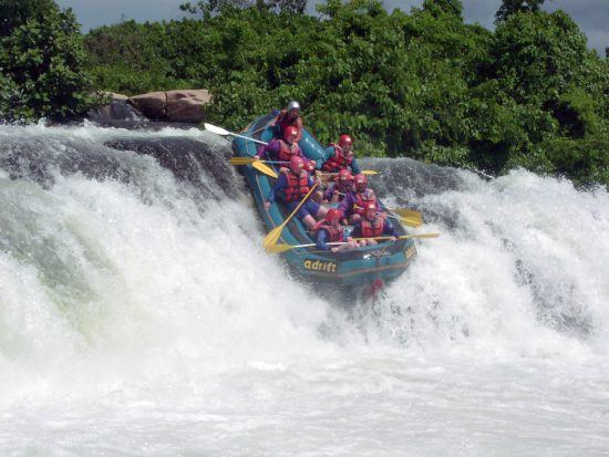 Eine Gruppe mit roten Helmen stürtzt sich beim Rafting in Uganda eine Stromschnelle hinunter