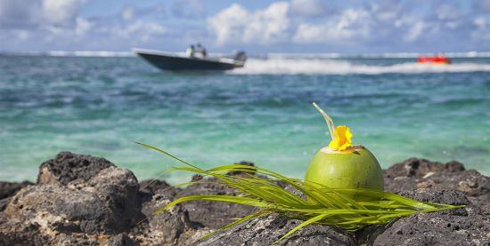 Kokosnuss zum Trinken auf Felsen mit Speedboot im türkisblauen Wasser im Hintergrund - Reiseführer Mauritius