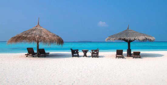 Zwei Sonnenschirmen und Sonnenliegen an einem weißen Sandstrand am glasklaren Meer