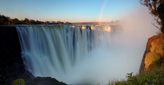 Das Wasser der Victoria-Fälle stürzt in die Tiefe und Sprühwasser bildet sich vor dem blauen Himmel - 8 Gründe, nach Sambia zu reisen