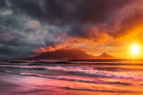 Ein farbintensiver Sonnenuntergang in Kapstadt mit dem Tafelberg und Lion's Head als dunkle Silhouetten