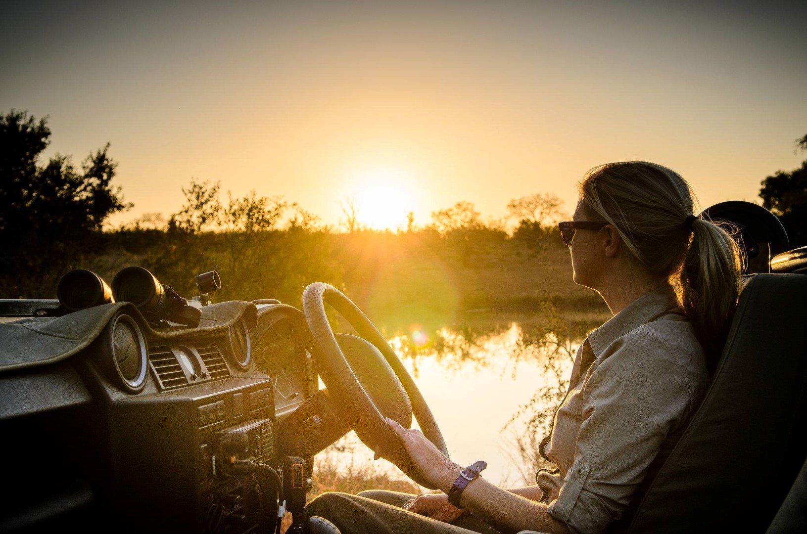 Jeune femme conduisant une voiture de safari au soleil levant dans la brousse. 