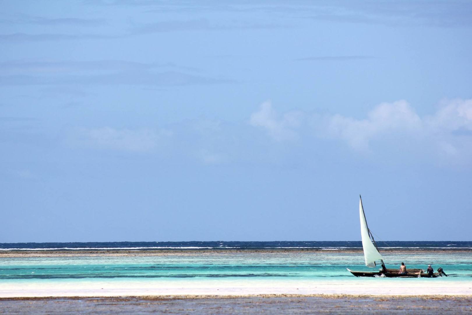 Weißer Sandstrand und dahinter türkisblaues Meer sowie ein Dhow