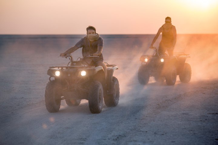 Zwei junge Männer düsen bei Sonnenuntergang auf Quad Bikes durch die Wüste