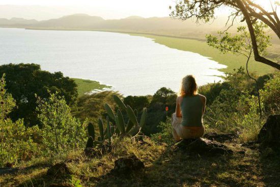 Frau sitzt auf einem Stein und genießt den Blick über einen See in Kenia