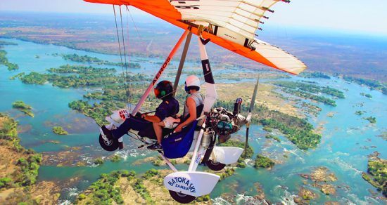 Zwei Personen fliegen in einem Ultraleichtflugzeug über die Victoria-Fälle in Sambia