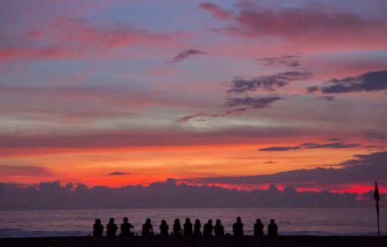 Gruppe sitzt am Strand bei Sonnenuntergang