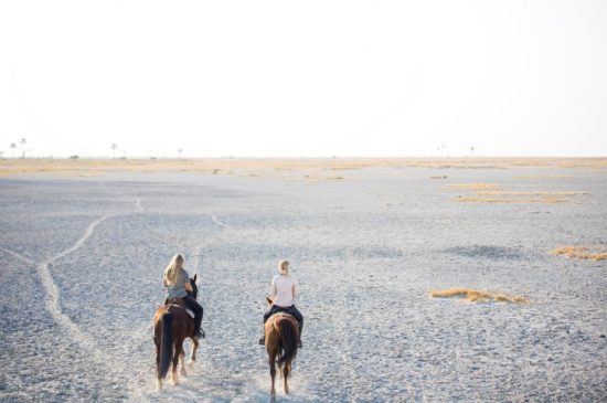 Zwei Frauen reiten in den weißen, kargen Makgadikgadi Salzpfannen aus