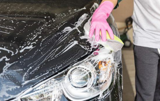 Mann mit pinkem Handschuh wäscht ein schwarzes Auto