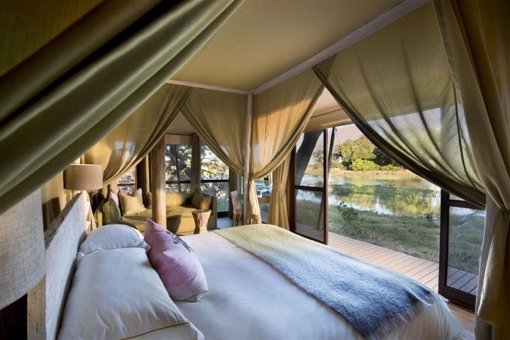 Freshly-made bed in an open tent overlooking a water landscape