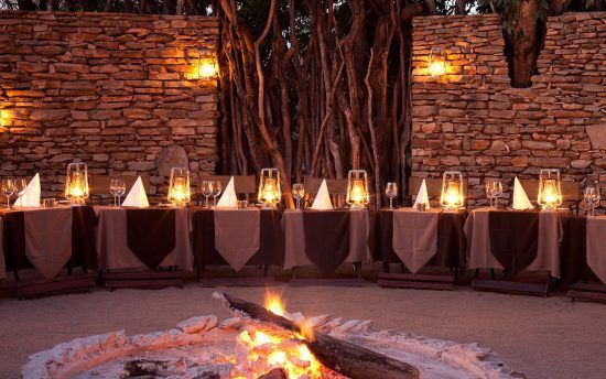 Dinner im Sabi Sand Game Reserve: Festlich gedeckte Tische in einer Boma mit Lagerfeuer in der Mitte