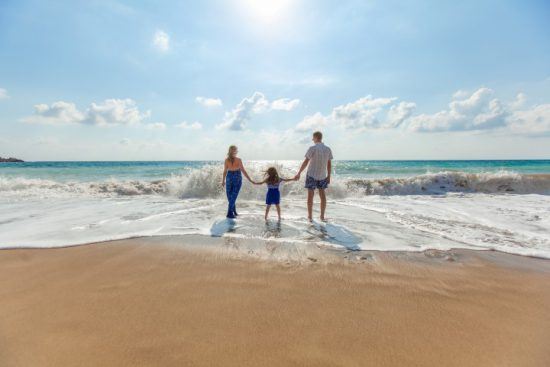 Mutter, Vater und Kind waten Hand in Hand in der Brandung an einem Sandstrand