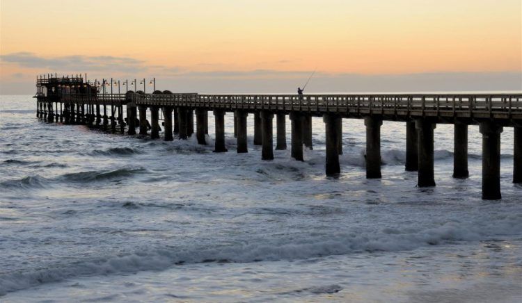 Ein Pier an einem traumhaften Strand vor einem farbenfrohen Sonnenuntergang in warmen Tönen