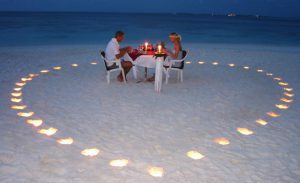 Ein Paar genießt ein romantisches Dinner am Strand umgeben von Kerzen, die ein Herz bilden