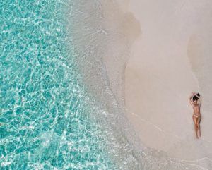 Eine Frau im Bikini liegt an ein einem einsamen Strand nahe der kristallklaren Brandung