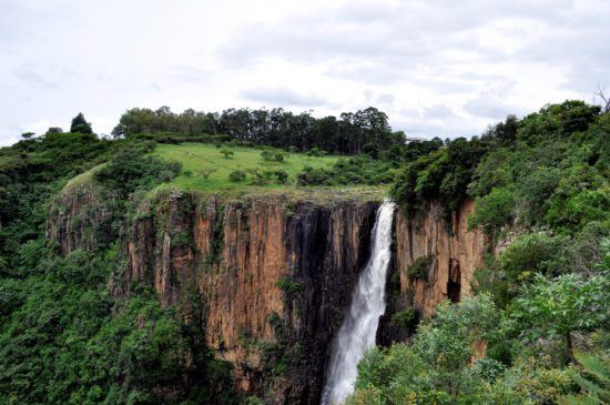 Ein Wasserfall zwischen rötlich-orangenen Felsen und grüner Natur - die schönsten Wasserfälle in Afrika