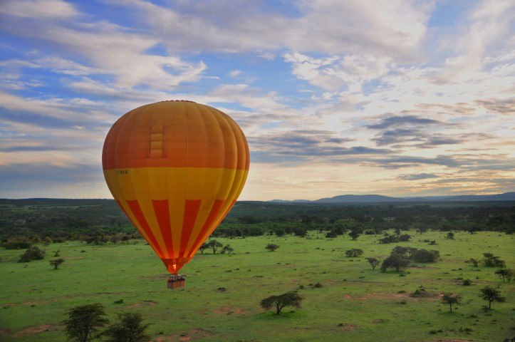 Ein gelb-orangener Heißluftballoon fliegt über den Krüger Nationalpark