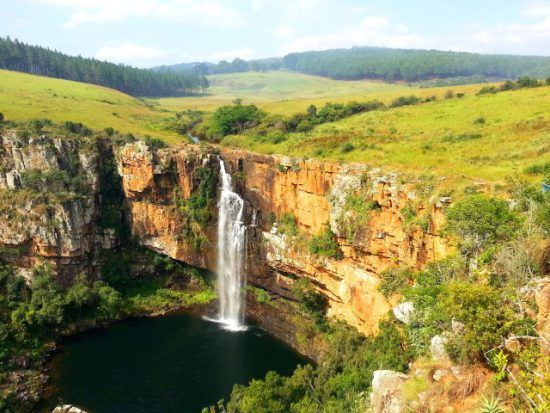 Der Berlin-Wasserfall stürzt sich zwischen grüner Graslandschaft und rötlichen Felsen in die Tiefe