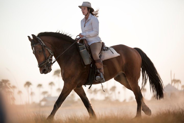 Eine Frau mit Hut reitet durch die afrikanische Wildnis