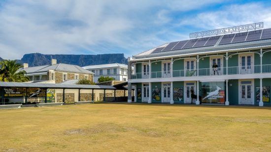 Ein türkises Haus, dahinter der Tafelberg, davor ein Sportrasen