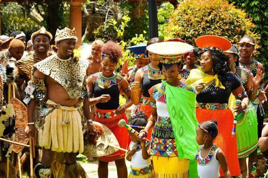 Zulus feiern eine traditionelle Hochzeit, vier Menschen im Vodergrund sind sehr bunt gekleidet