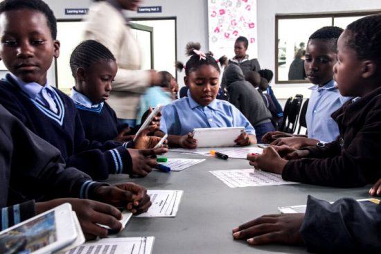 Kinder in blauer Schuluniform lernen mit Tablets am Justicia Campus der Good Work Foundation