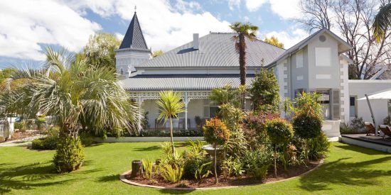 ein Gebäude im Kolonialstil, runherum ein grüner Garten