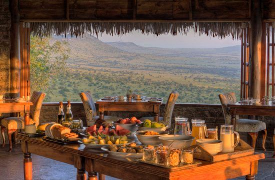 Im Vordergrund ein Frühstücksbuffet, dahinter ein Tisch mit Ausblick auf die Savanne