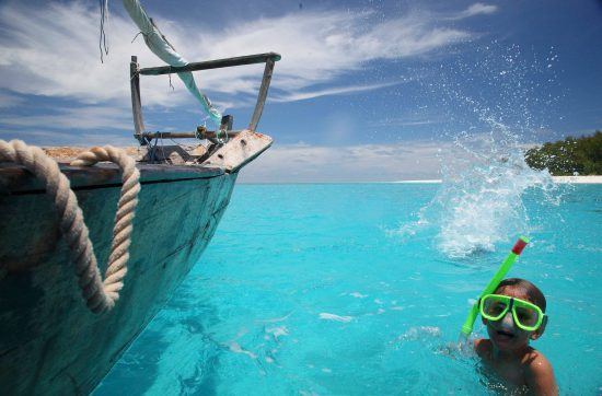 ein Kind mit Taucherbrille im Meer neben einem Boot in Sansibar