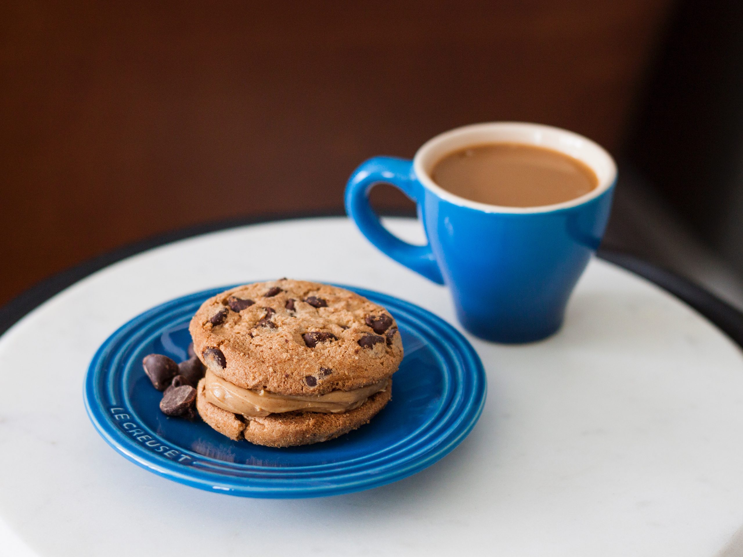 A steaming cup of coffee and a blue plate of choc-chip cookies