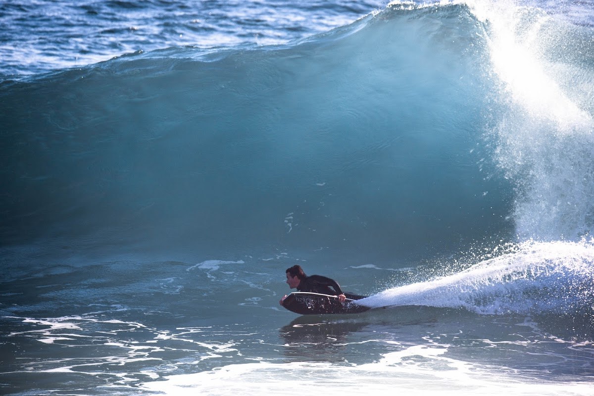 Tall, blue wave begins to curl over a surfer in Cape Town