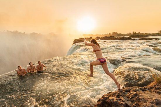 Eine Frau springt bei Sonnenuntergang in den Devil's Pool bei den Victoria-Fällen