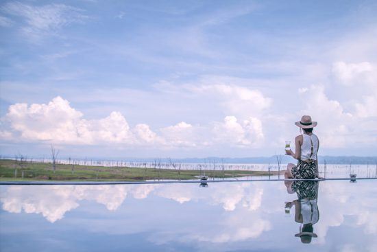 Eine Frau sitzt am Beckenrand eines Infinity-Pools und blickt auf den Lake Kariba