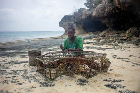 Ein Angler flickt am Strand von Sansibar seine Netze