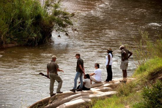 Safari-Urlauber auf einer Buschwanderung im Lion Sands Game Reserve an einem Fluss