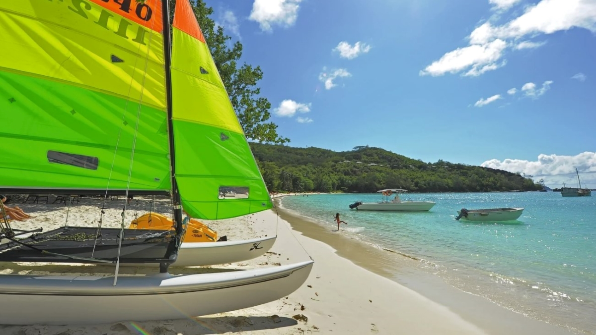 Beach with child playing in the waves with boats in the foreground and background