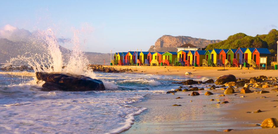 Wave splashing on rock at St James Beach with colorful huts, Cape Town, South Africa