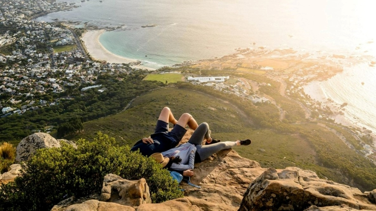 A couple relaxing on a mountain edge looking over Cape Town's beaches