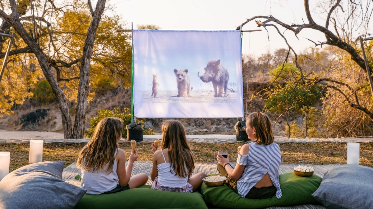 Three children watching the Lion King via projector and screen out in the open bush