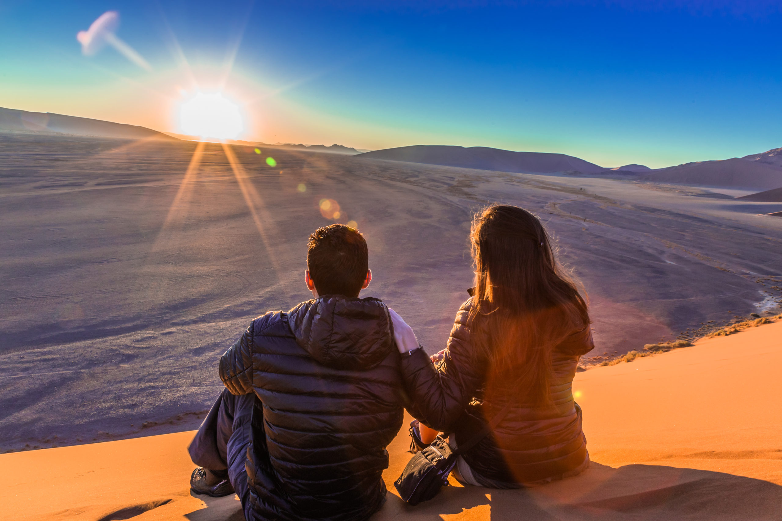 Couple on sand dune in desert during sunrise.  Sossusvlei, Namib