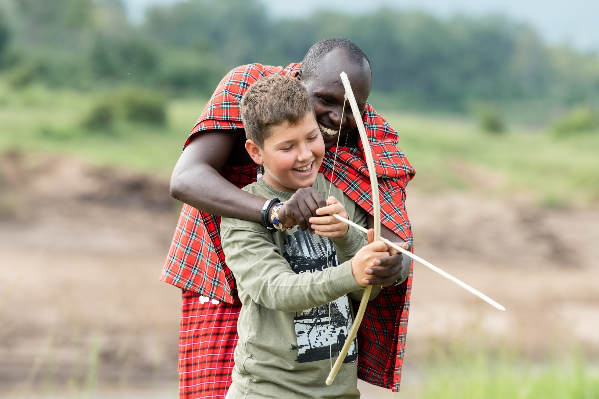 Maasai warrior teaching bow and arrow skills to a teenage boy