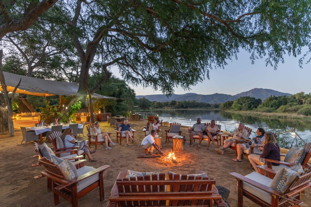 Family sitting around a bonfire alongside a river