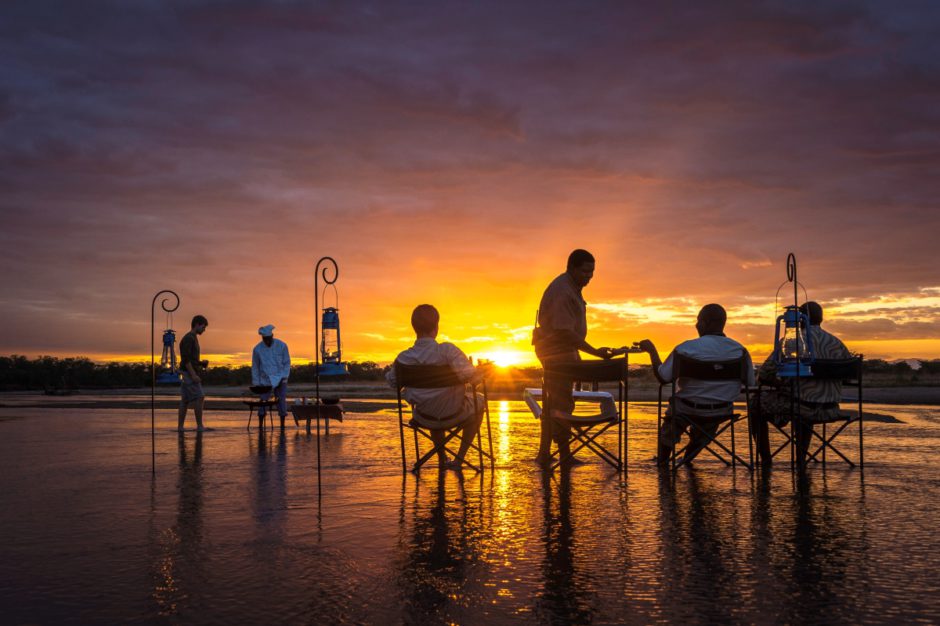 Guests enjoying drinks and snacks sitting on the shallow waters of the river at sunset